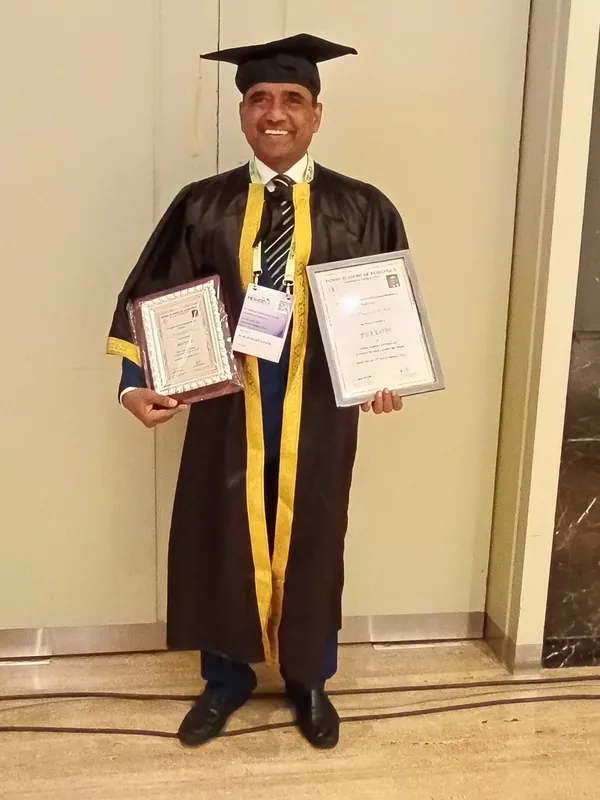 Dr. Ramakant Patil standing in black-and-gold academic regalia and cap, holding two framed certificates.